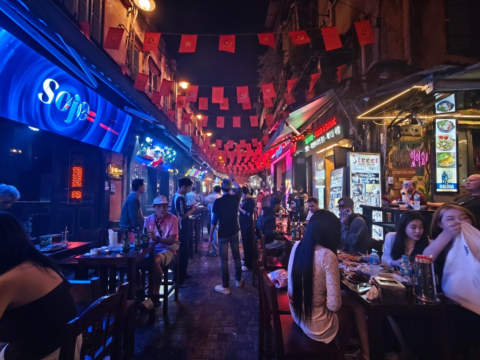 Nocna uliczna scena z restauracjami i ludźmi.