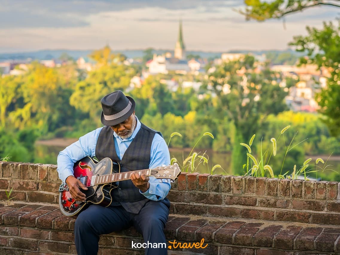 Starszy mężczyzna gra na gitarze, malowniczy widok miasta o zachodzie słońca.