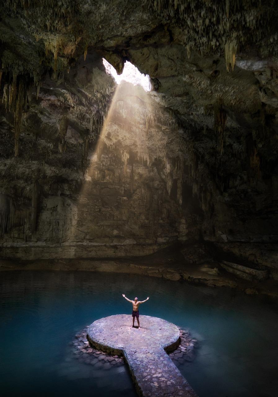 Mężczyzna z rozłożonymi rękami w jaskini cenote oświetlonej słońcem.