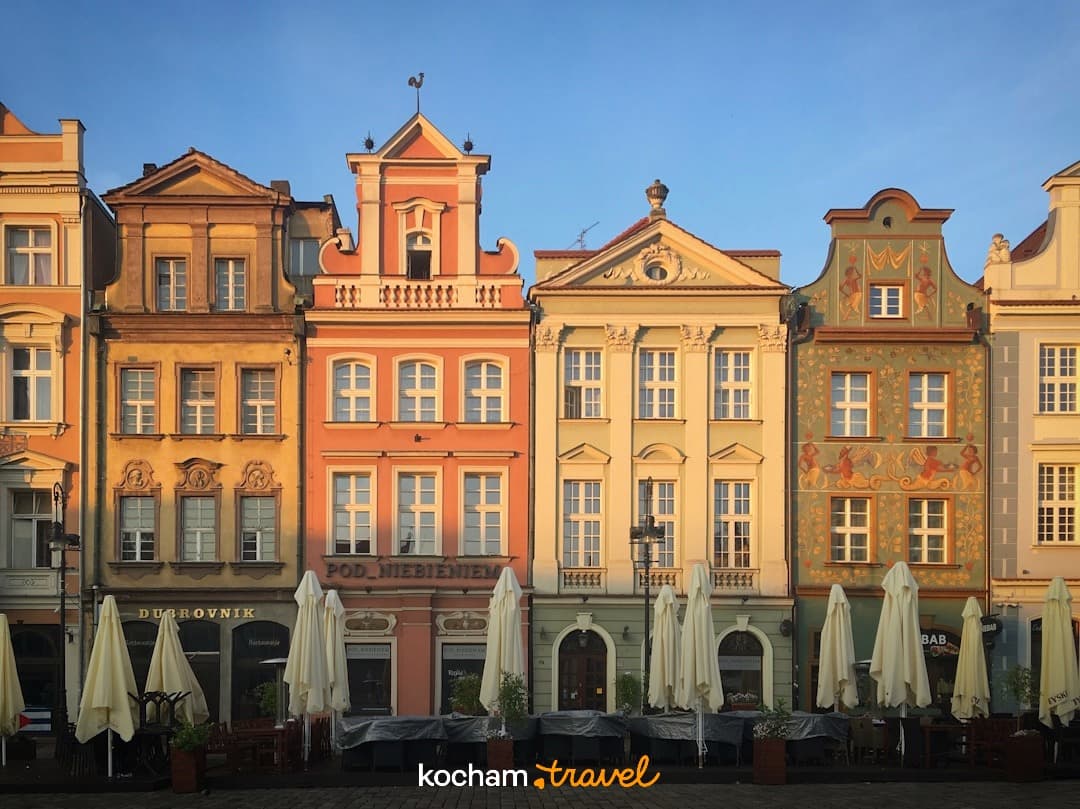 Zabytkowe kolorowe kamienice na rynku z parasolami i kawiarniami.