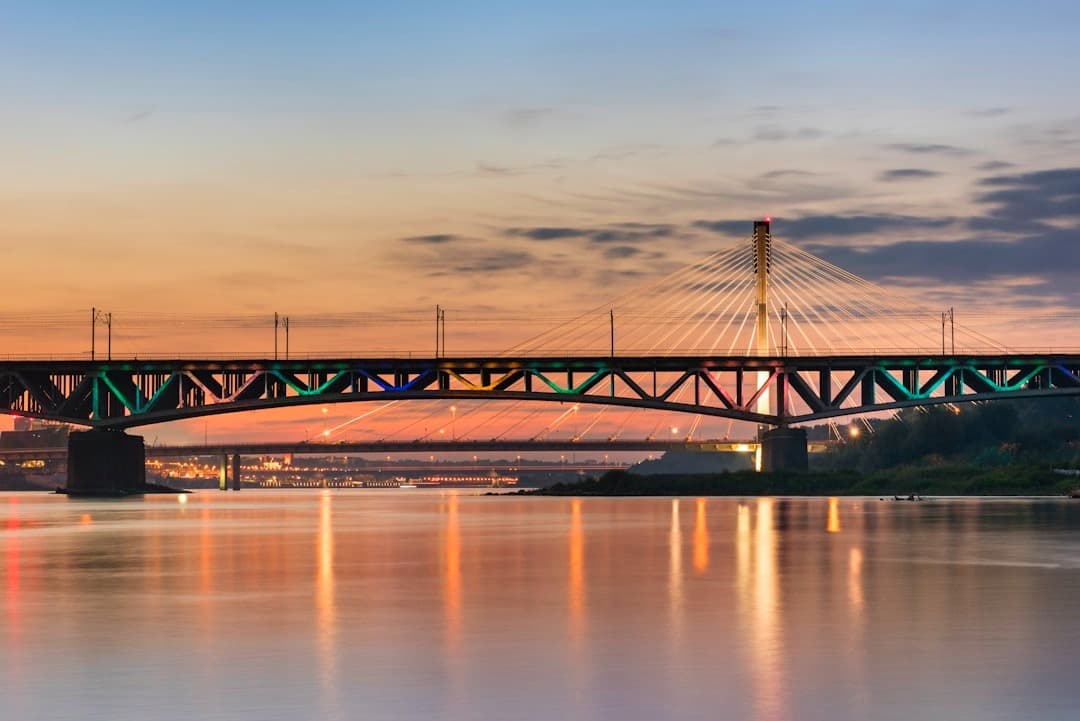 Oświetlone mosty nad rzeką o zachodzie słońca, odbicia świateł miasta.