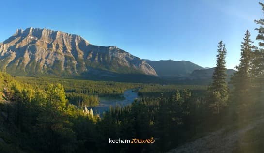 Panoramiczny górski krajobraz z turkusową rzeką i lasem o zachodzie słońca.