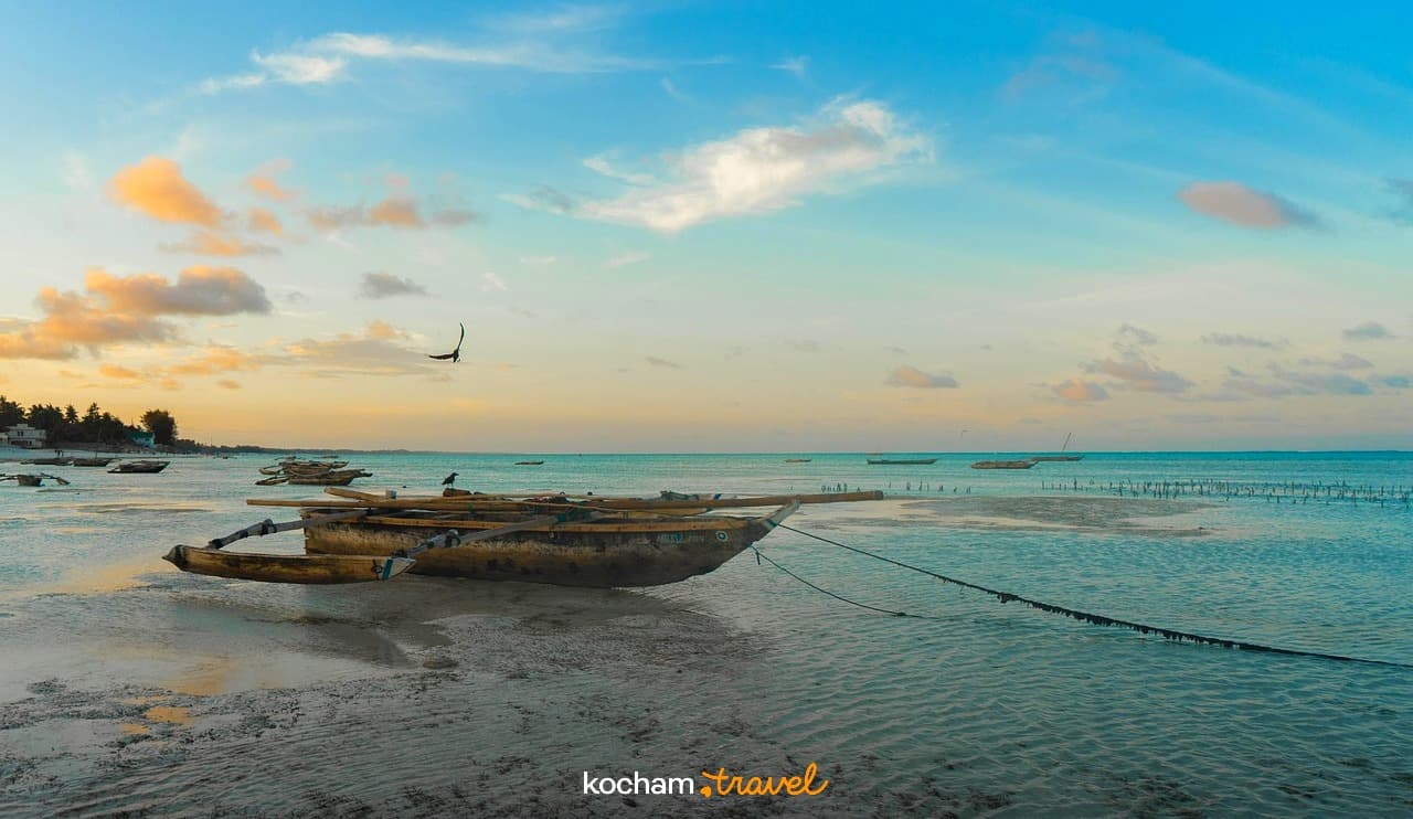 Tradycyjne łodzie na piaszczystej plaży, turkusowy ocean, zachód słońca.