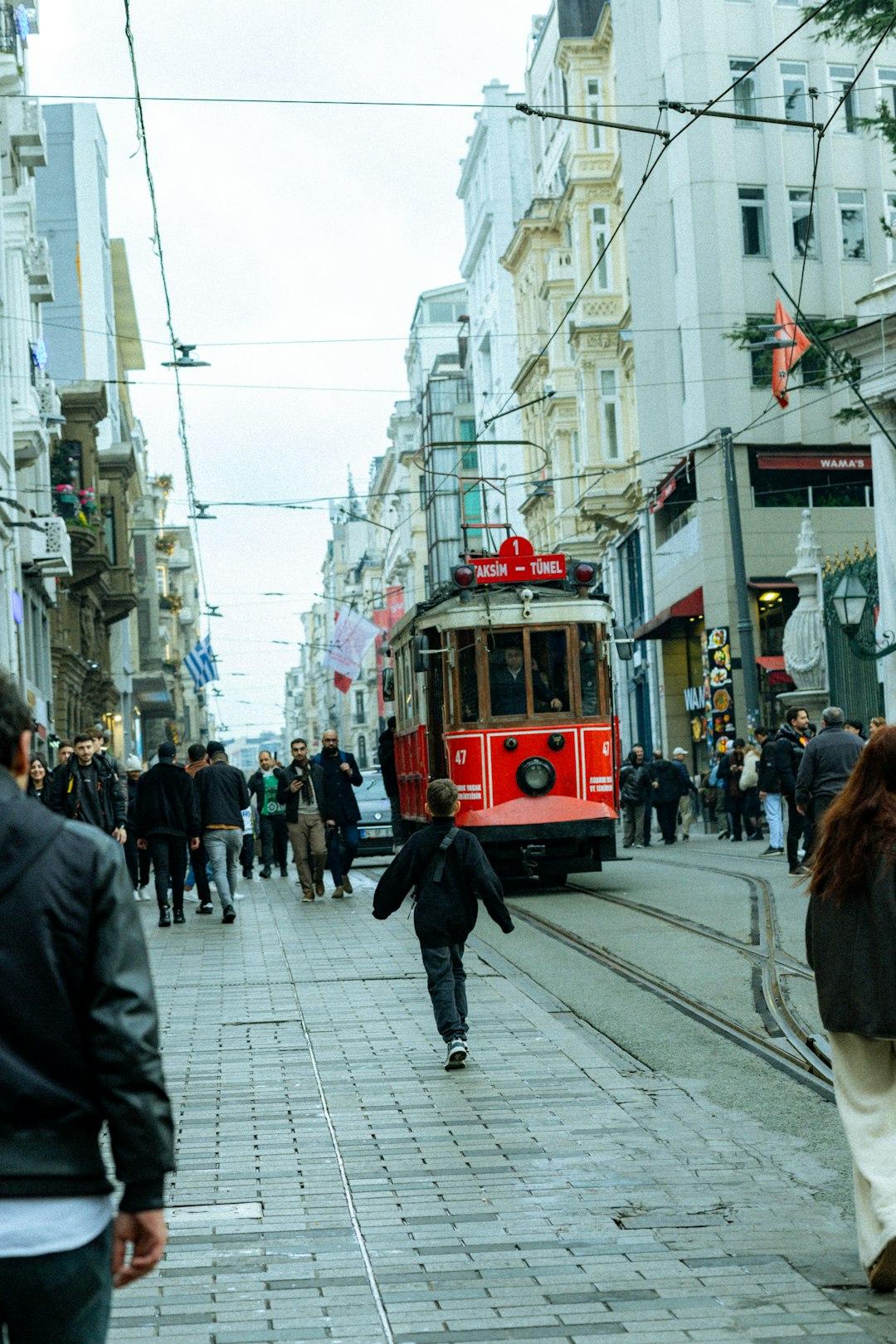 Czerwony historyczny tramwaj na brukowanej ulicy Istambułu wśród pieszych.