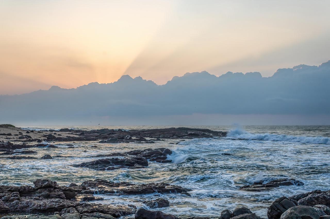 Skaliste wybrzeże oceanu z falami i promieniami słońca przez chmury.