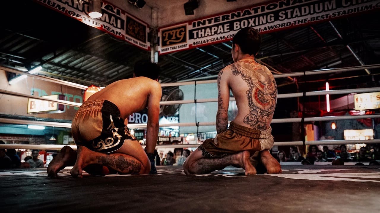 Zawodnicy Muay Thai z tatuażami klęczący w ringu bokserskim w Tajlandii.
