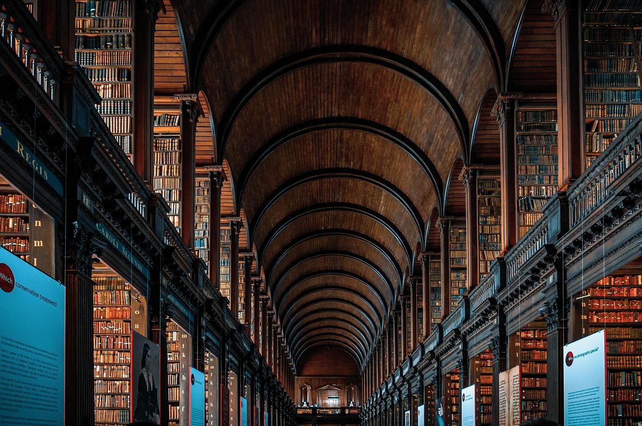 Wnętrze zabytkowej biblioteki z długą salą, regałami i drewnianym sklepieniem.