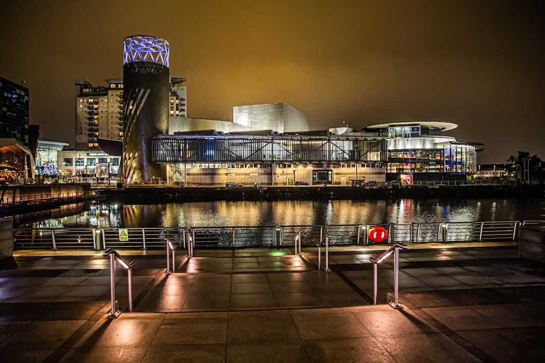 Oświetlone nowoczesne budynki MediaCityUK odbijające się w wodzie nocą.