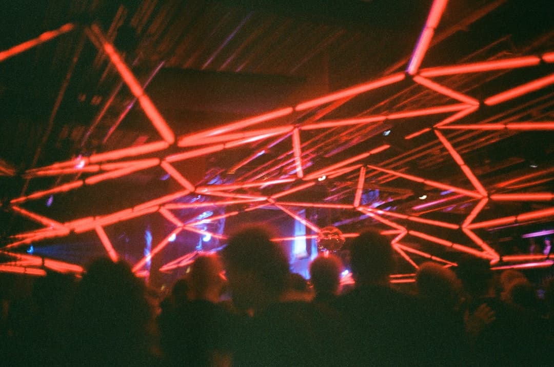 Tłum ludzi tańczących pod czerwonymi neonami i kulą disco.