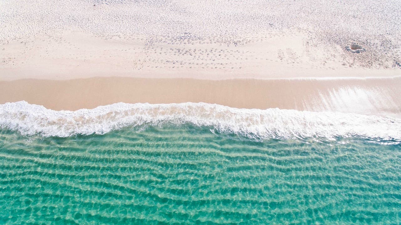 Widok z lotu ptaka: turkusowy ocean, biały piasek, fale.