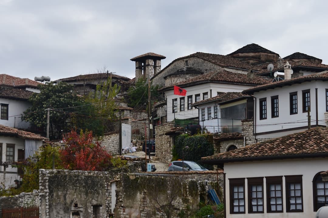 Historyczny Berat, Albania, tradycyjne białe domy, brązowe dachy, kamienne mury, albańska flaga.