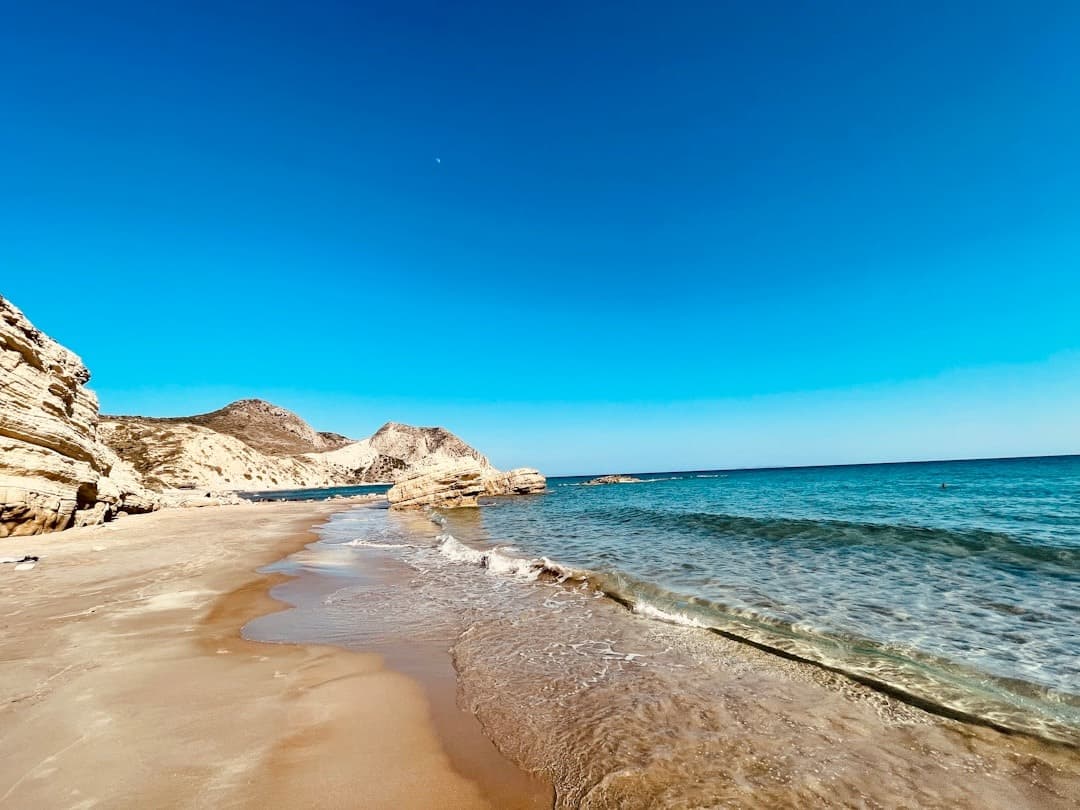 Piaszczysta plaża, turkusowe morze, skaliste klify, słoneczny dzień.