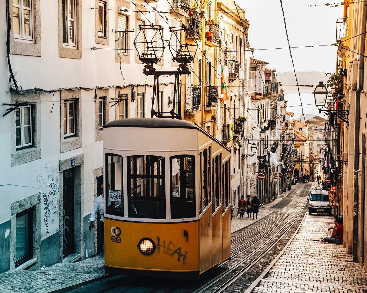 Ikoniczny żółty tramwaj w Lizbonie, stroma brukowana ulica, zachód słońca.