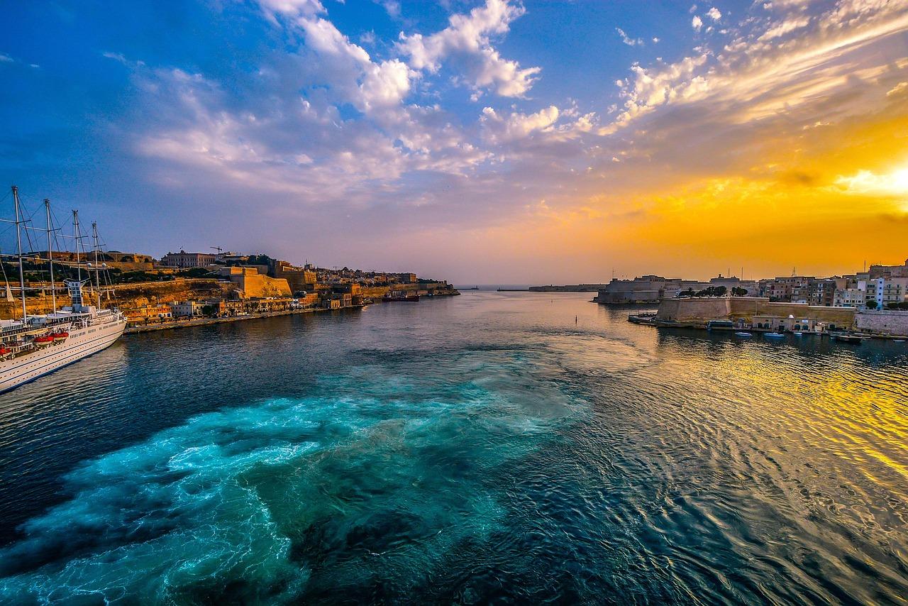 Maltański port Grand Harbour o zachodzie słońca ze statkiem i fortyfikacjami.