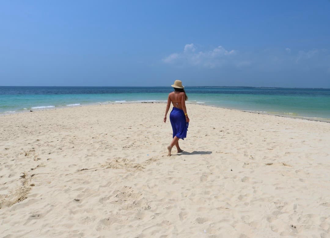 Kobieta spacerująca po białej piaszczystej plaży z turkusową wodą.