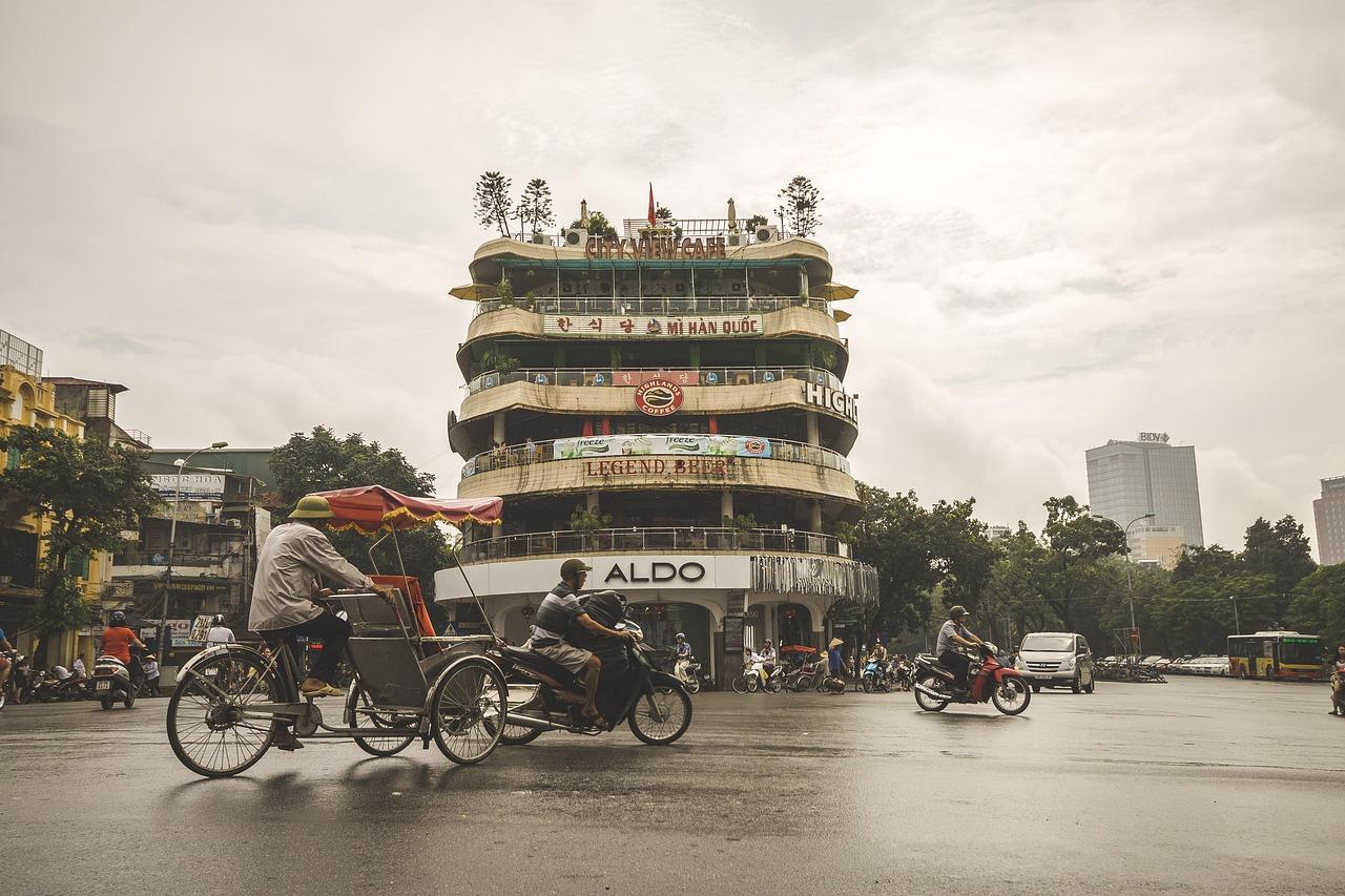 Ruchliwa ulica w Hanoi, Wietnam, z budynkiem, motocyklami i rikszami.