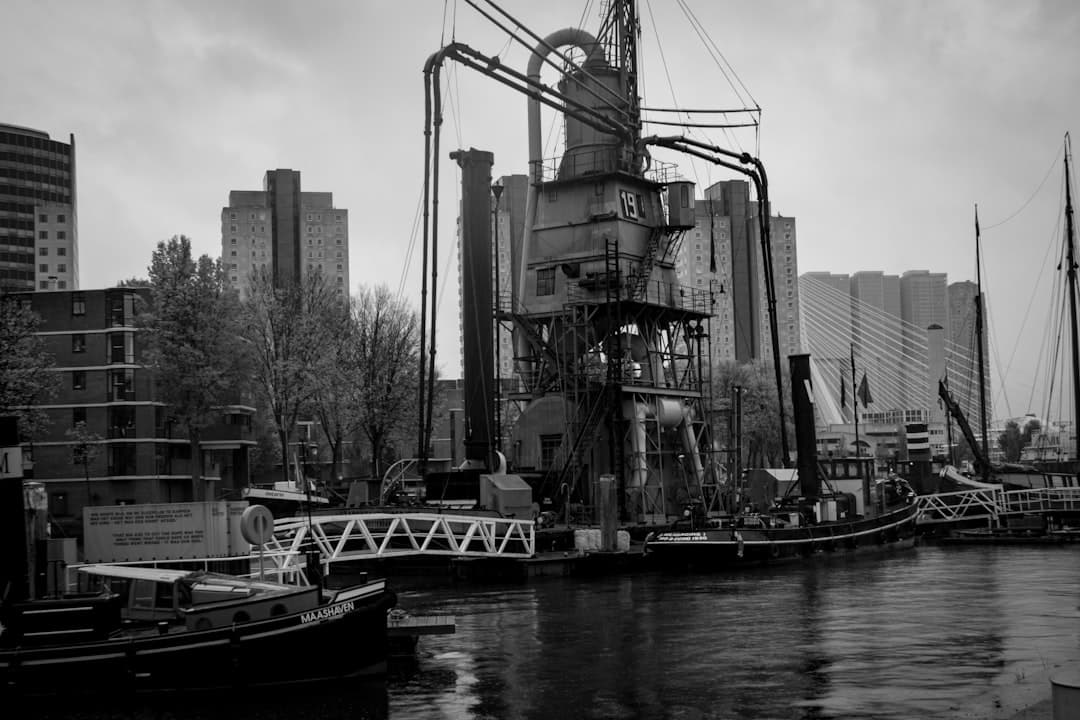 Przemysłowy port w Rotterdamie z żurawiem, barkami i mostem Erasmus.