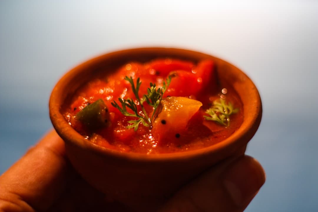 Czerwony, owocowo-warzywny chutney w glinianej miseczce z ziołami.