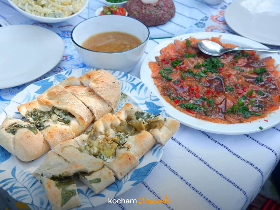 Różne dania na stole: podpłomyki, carpaccio z łososia, zupa, sałatka ziemniaczana.