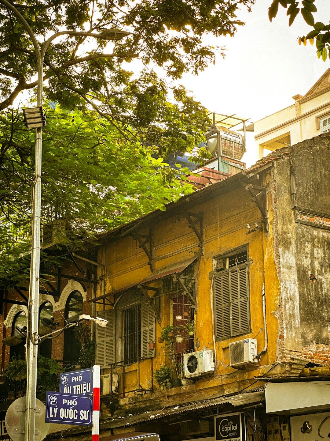 Ulica w Hanoi z zabytkowym żółtym budynkiem i zielonymi drzewami.