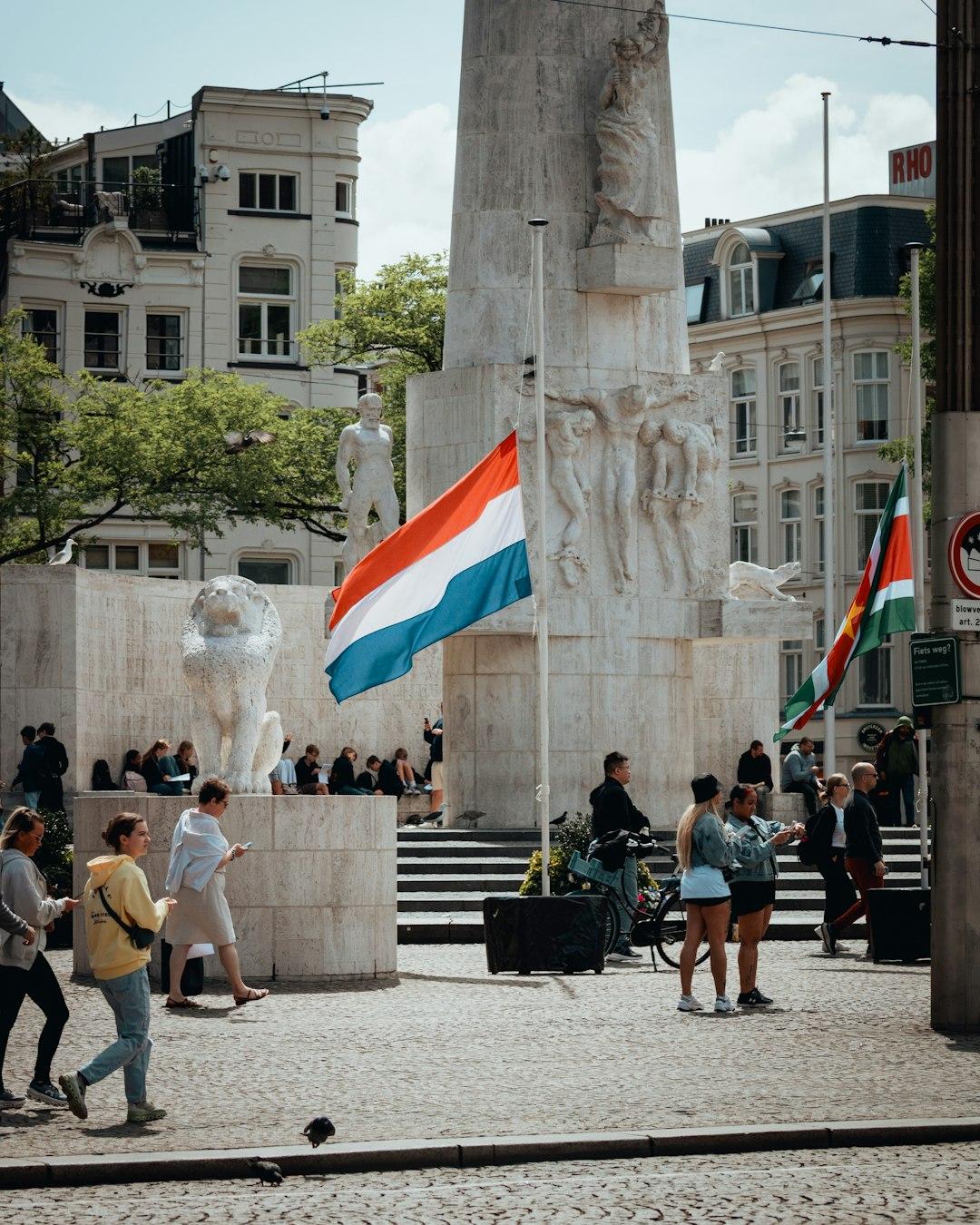 Narodowy Pomnik w Amsterdamie na Placu Dam z powiewającą holenderską flagą.