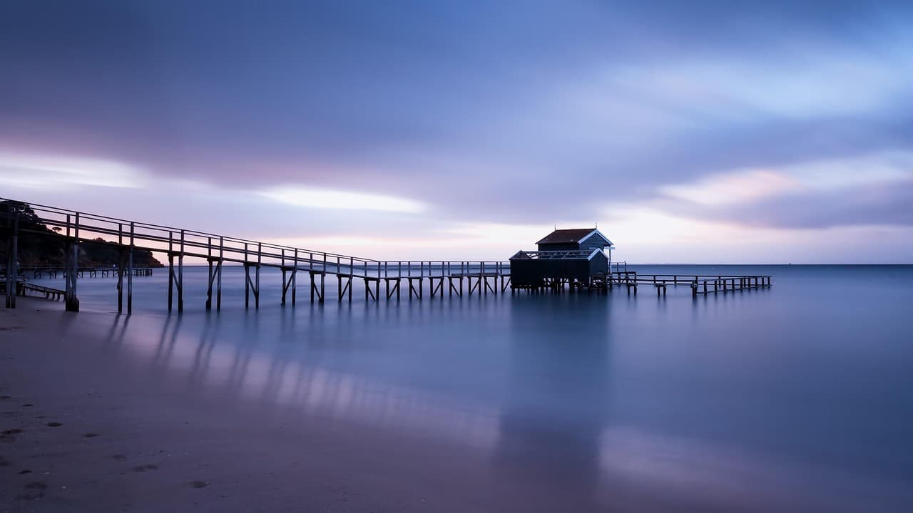 Molo z domkiem nad wodą, zachód słońca, spokojna plaża.