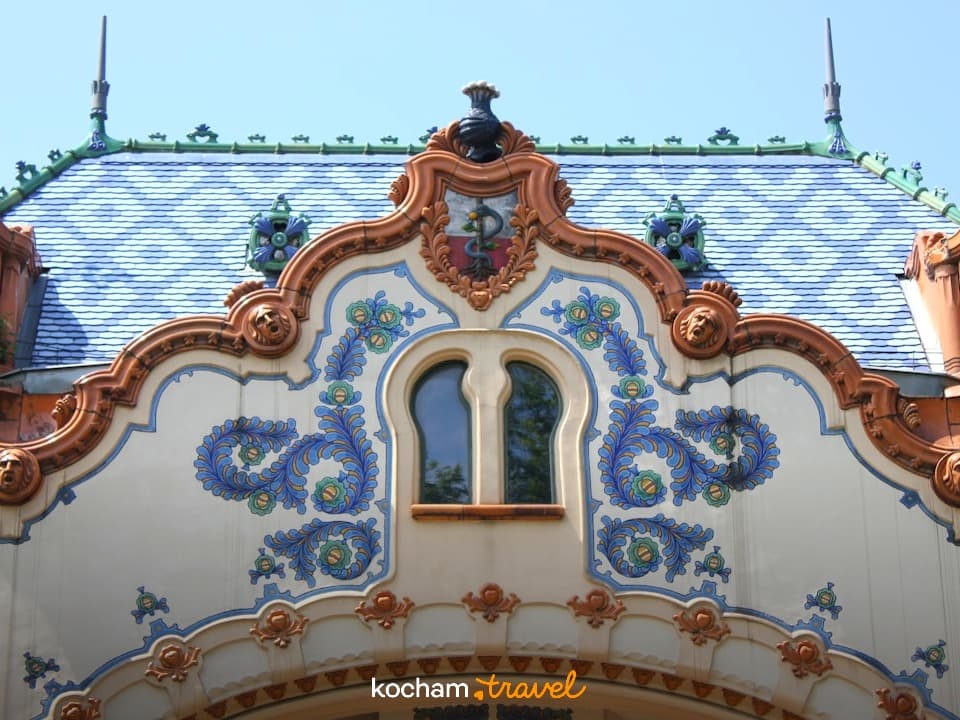 Bogato zdobiona fasada, niebiesko-biały dach, ornamenty, okno, motyw węża.