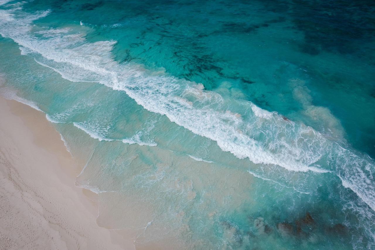Widok z góry na turkusowe fale oceanu i piaszczystą plażę.