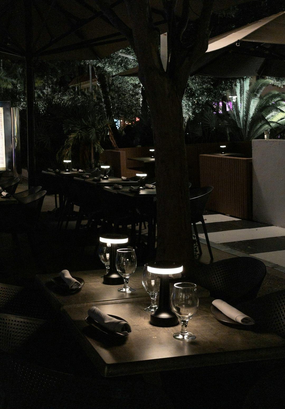 Nastrojowa restauracja na świeżym powietrzu wieczorem z oświetlonymi stolikami i zielenią.