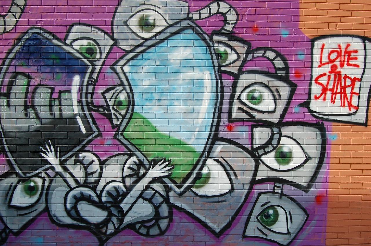 Kolorowe graffiti z oczami, kształtami i napisem "LOVE & SHARE" na murze.