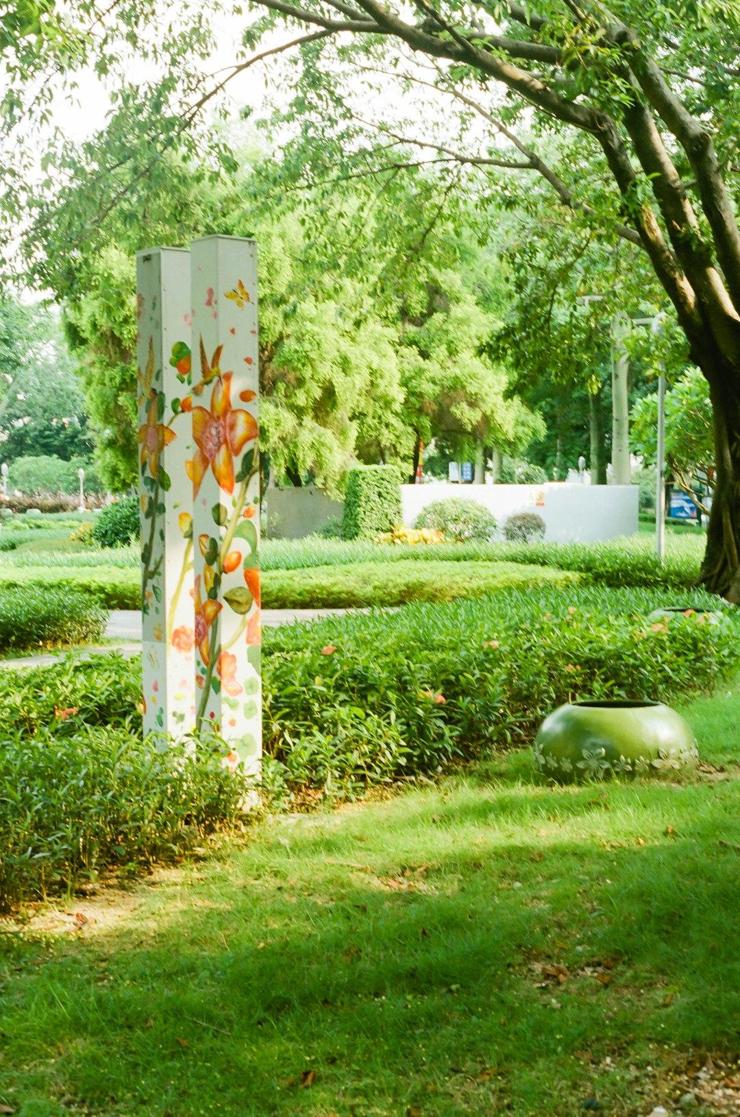 Zielony park ze słupkiem z malowanymi kwiatami i donicą.