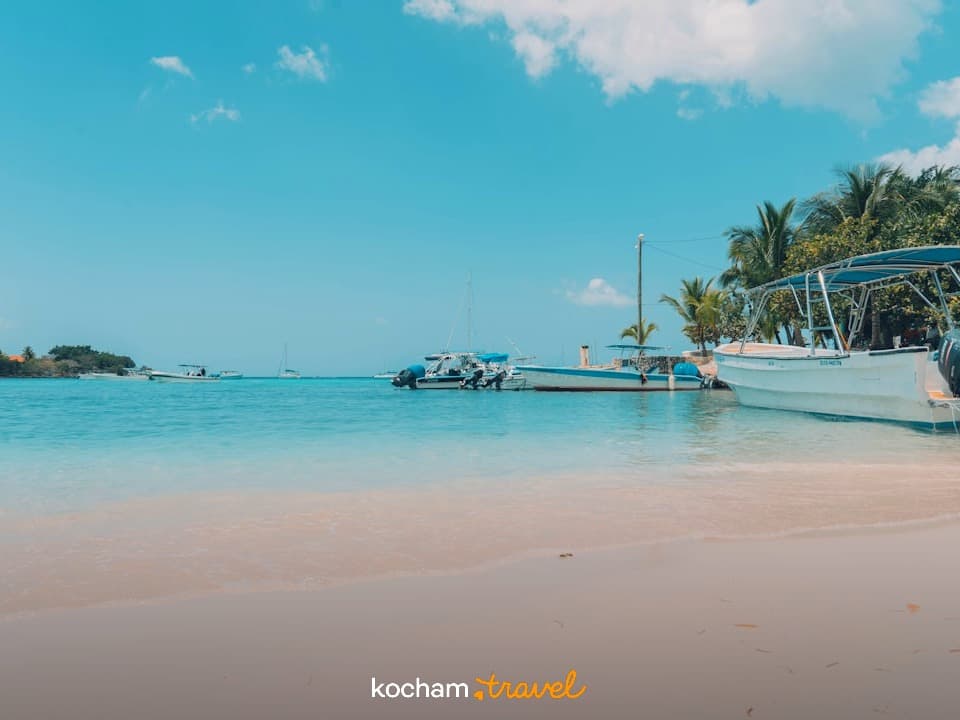 Tropikalna plaża z turkusową wodą, łodziami i palmami w słoneczny dzień.