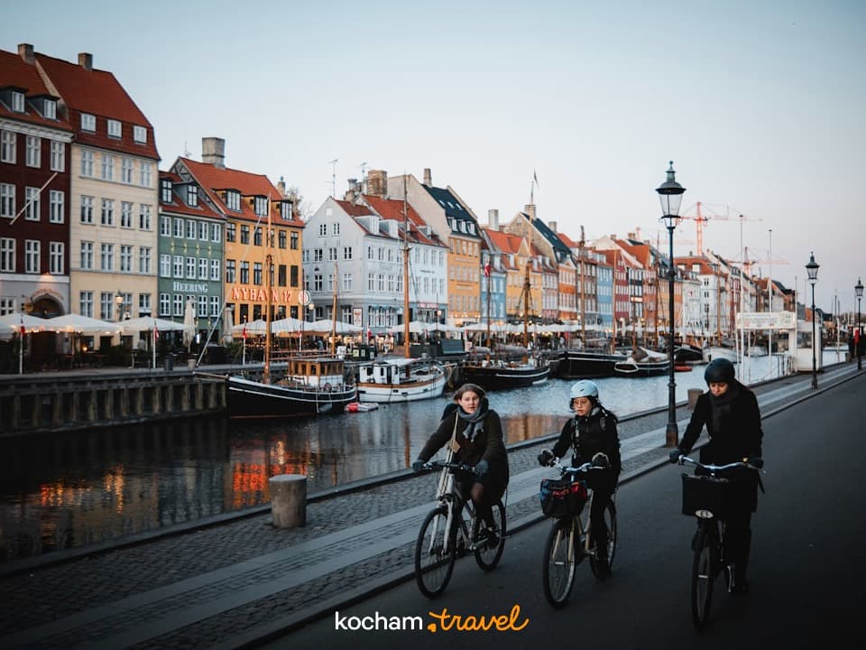 Ludzie jadący rowerami wzdłuż kanału Nyhavn z kolorowymi budynkami Kopenhagi.