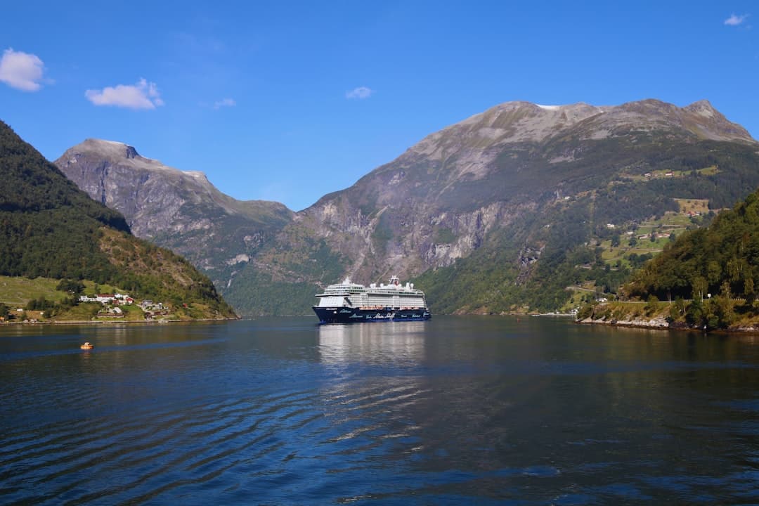 Statek wycieczkowy w fiordzie norweskim otoczony zielonymi górami.