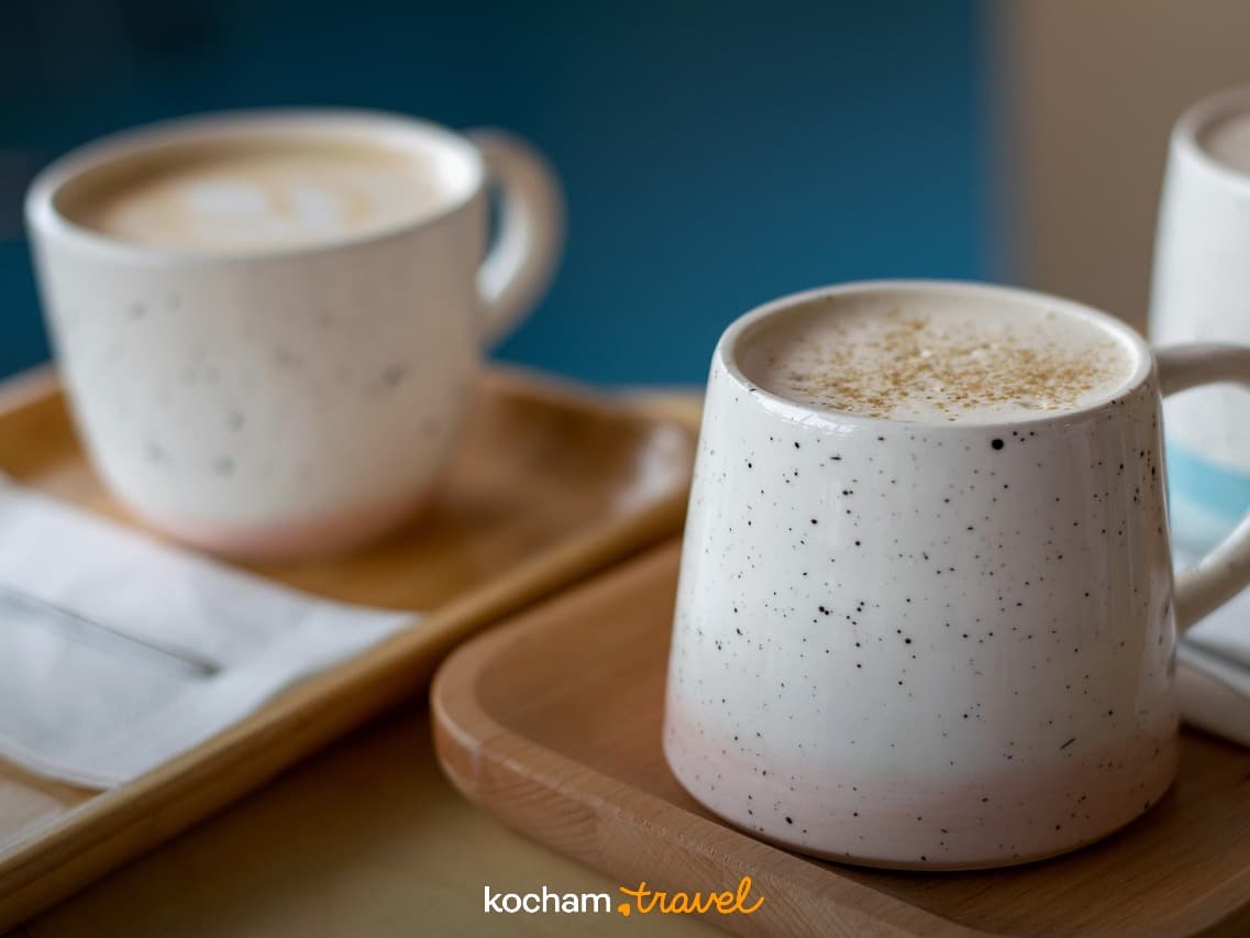 Dwie ceramiczne filiżanki kawy latte na drewnianych tacach.