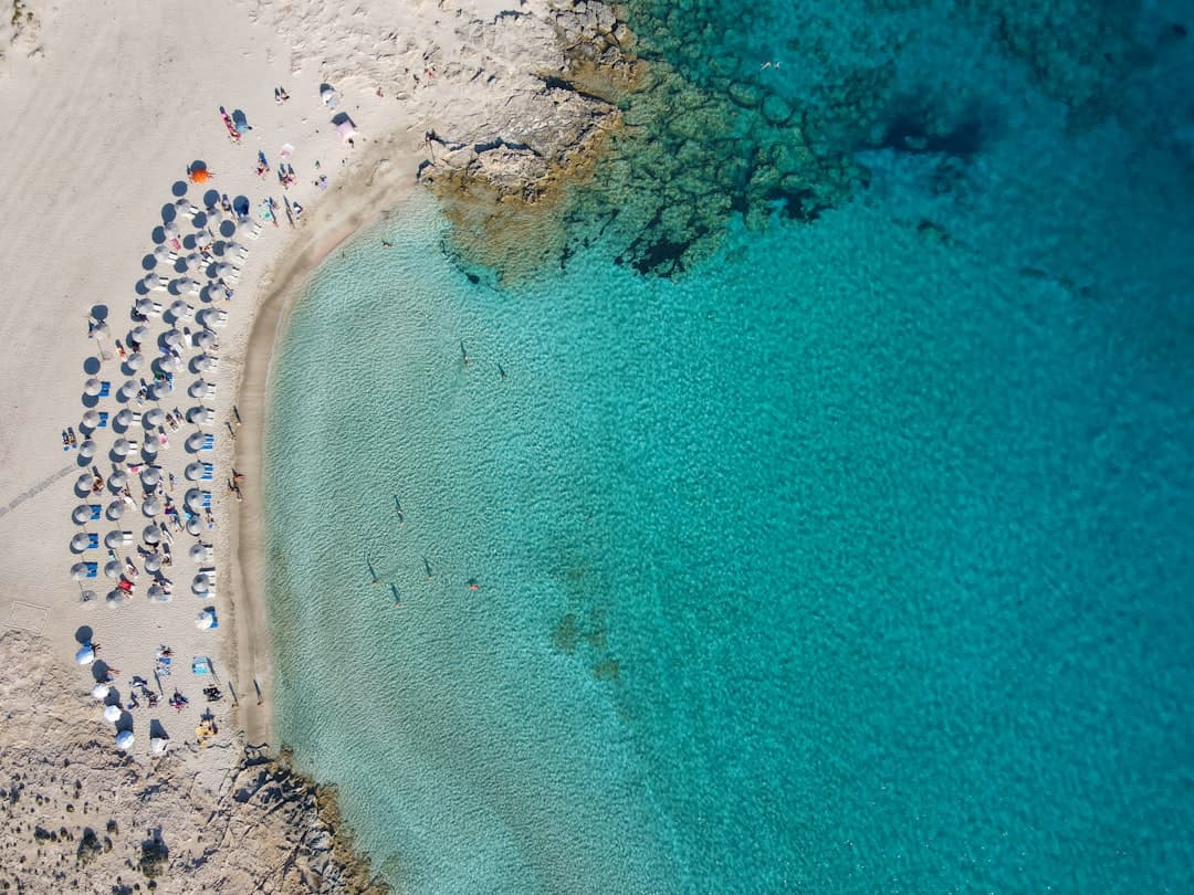Turkusowa zatoka, piaszczysta plaża, leżaki, parasole, kąpiący się ludzie.