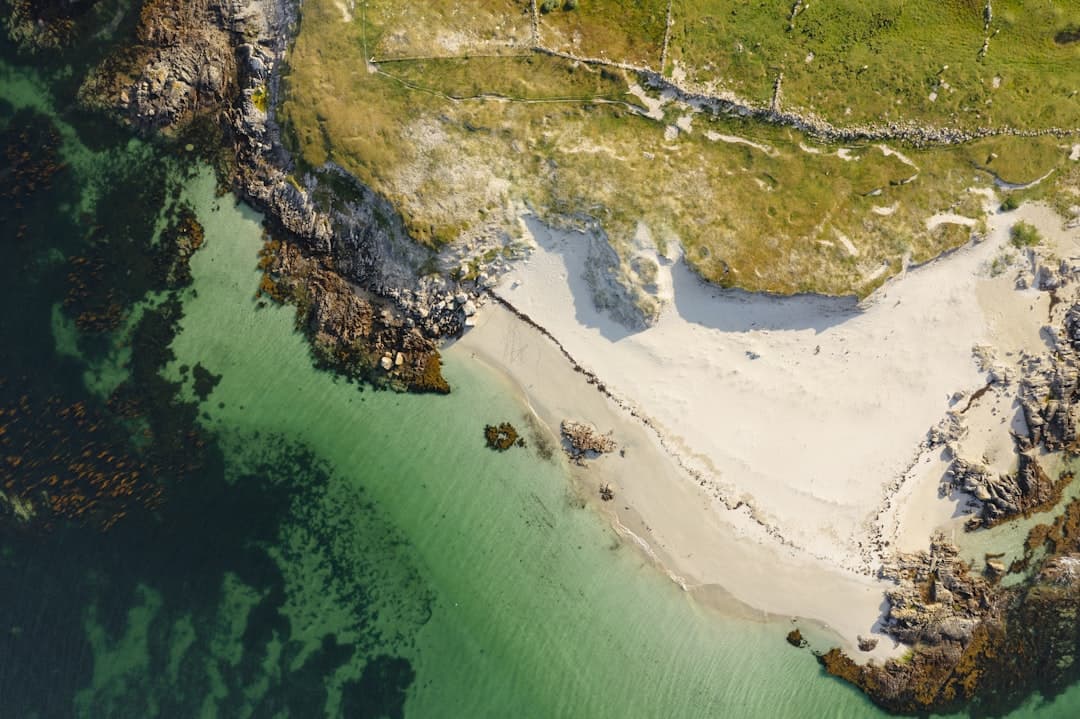 Piaszczysta plaża, turkusowa woda, skaliste wybrzeże i zielone wydmy.