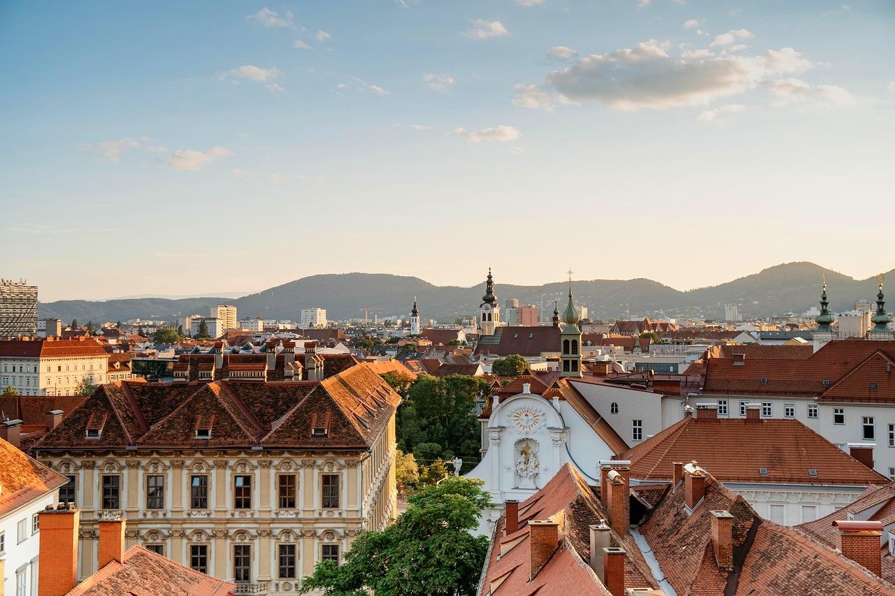 Panorama miasta, czerwone dachy, zabytkowa architektura, wieże kościelne, góry.
