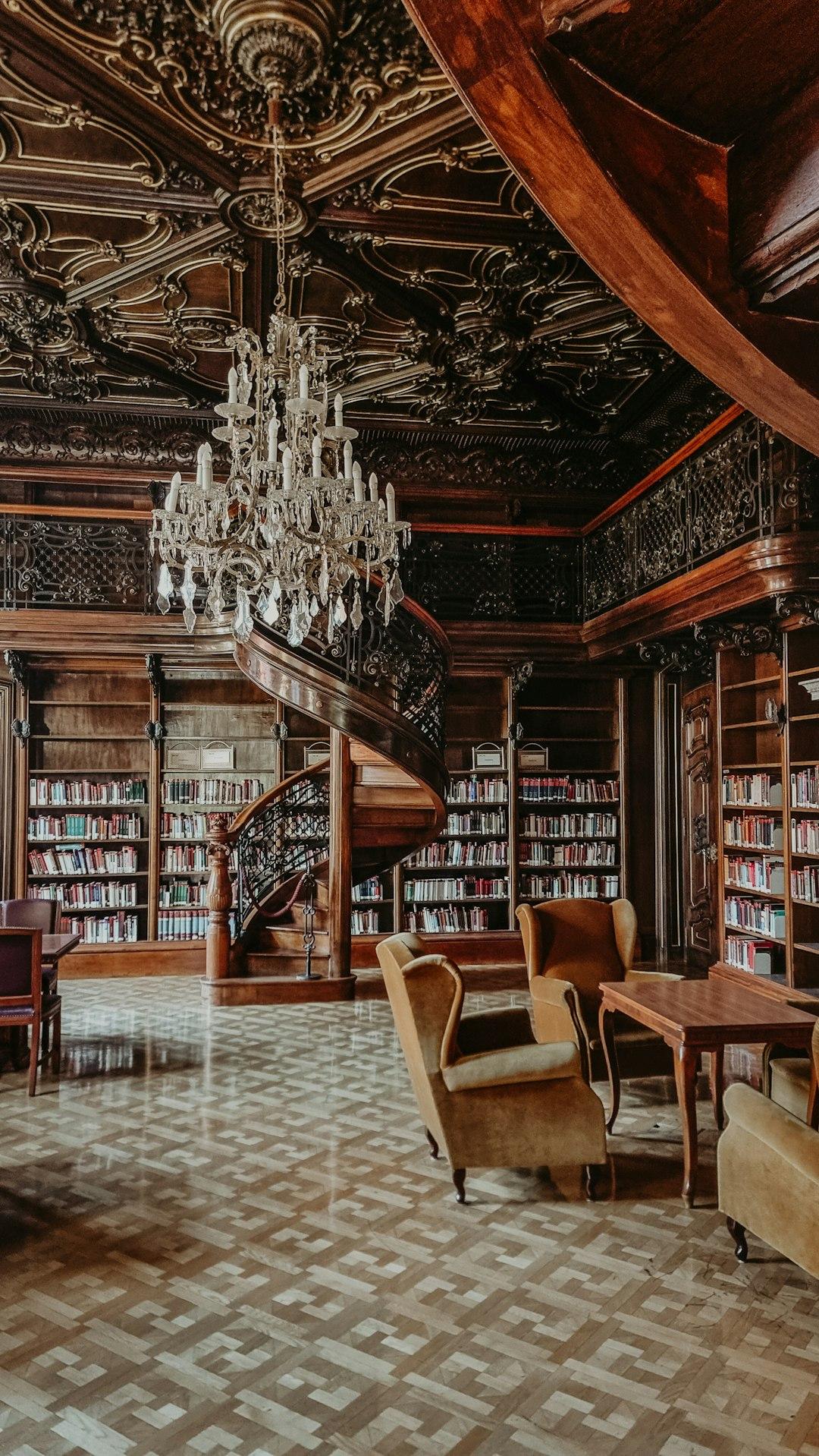 Wytworna, drewniana biblioteka ze spiralnymi schodami i żyrandolem kryształowym.