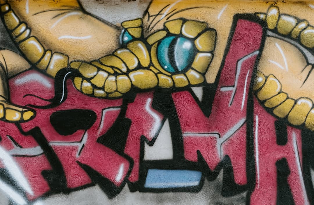 Kolorowe graffiti przedstawiające żółtego węża z niebieskim okiem na ścianie.
