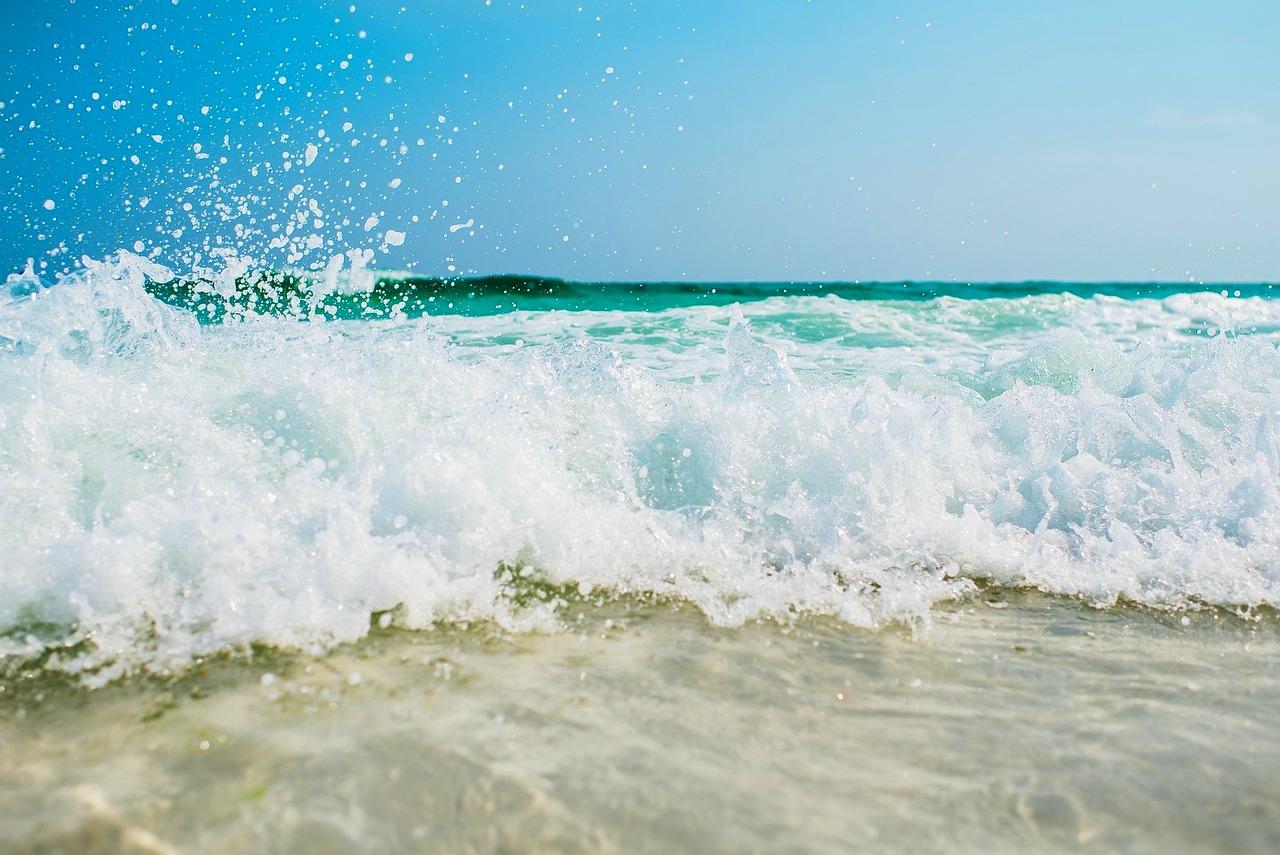Spieniona fala na turkusowym oceanie pod błękitnym niebem.