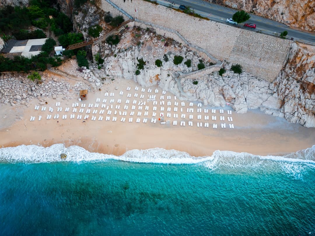 Piaszczysta plaża z rzędami leżaków, lazurowa woda i skaliste klify.