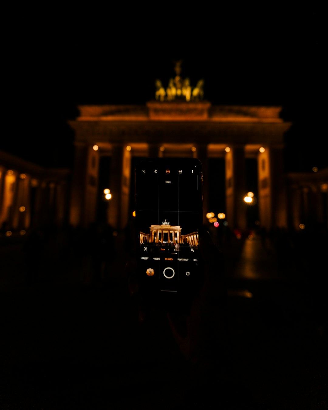 Smartfon fotografujący oświetloną Bramę Brandenburską w Berlinie nocą.