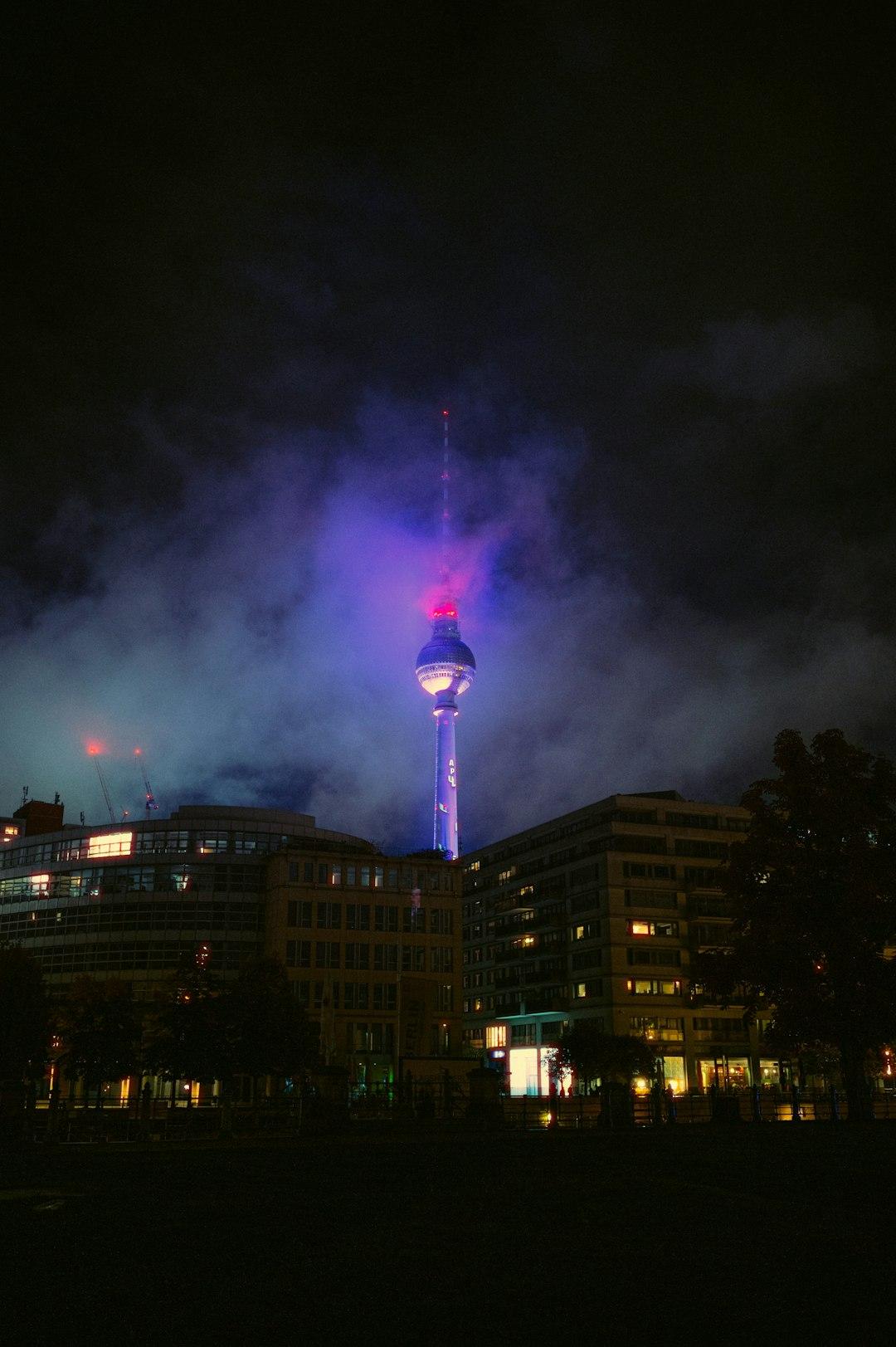 Berlińska Wieża Telewizyjna oświetlona fioletowo-różowo nocą, wśród mgły.