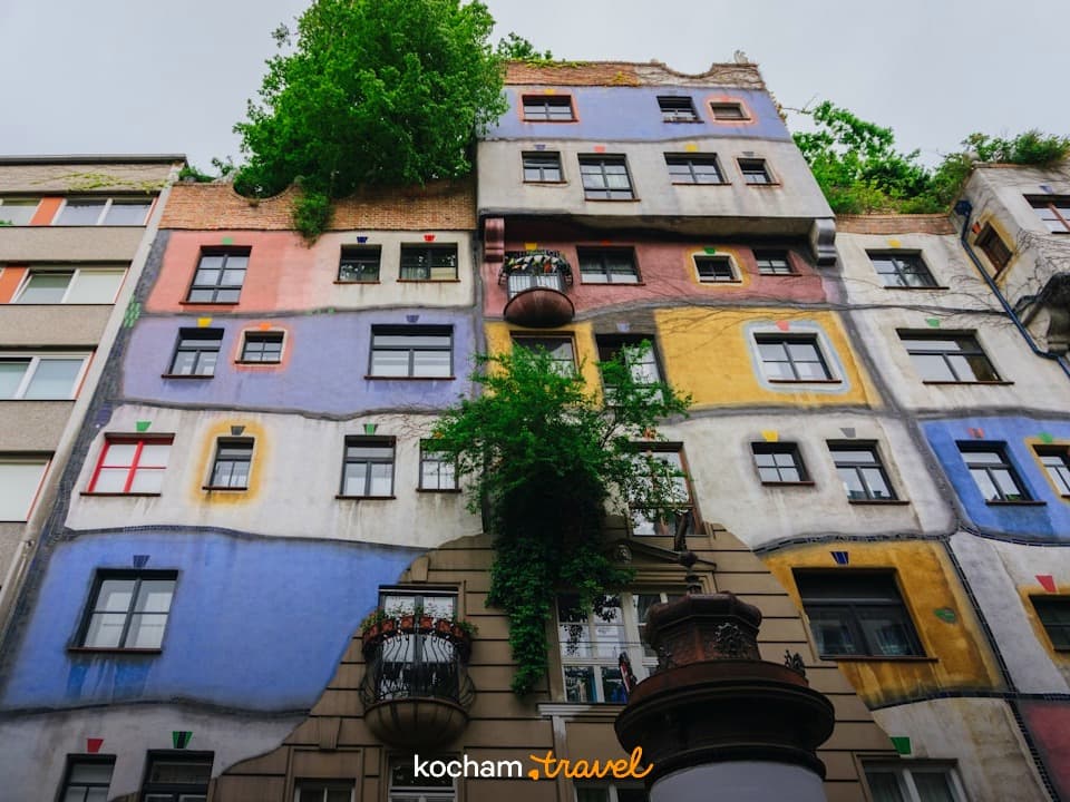 Unikalna, kolorowa fasada Hundertwasserhaus w Wiedniu, drzewa na budynku.