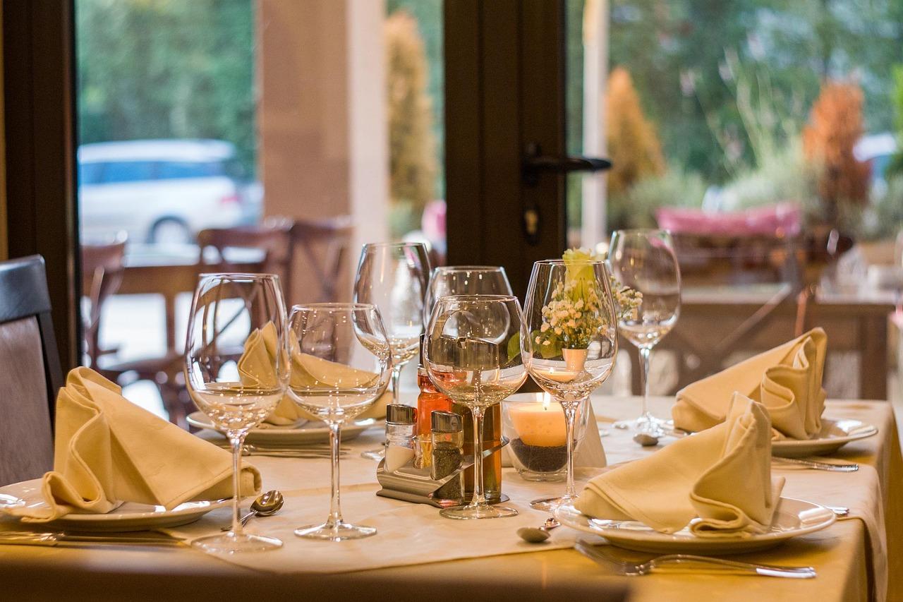 Stół w restauracji z kieliszkami, serwetkami, świecą i kwiatami.
