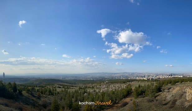 Panoramiczny widok na panoramę miasta z zalesionego wzgórza, jasne niebo, białe chmury.