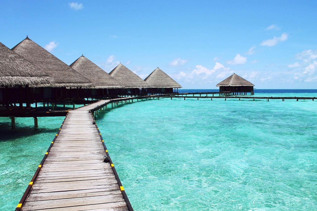 Tropikalne bungalowy na wodzie z dachami krytymi strzechą, turkusowy ocean, pomost.