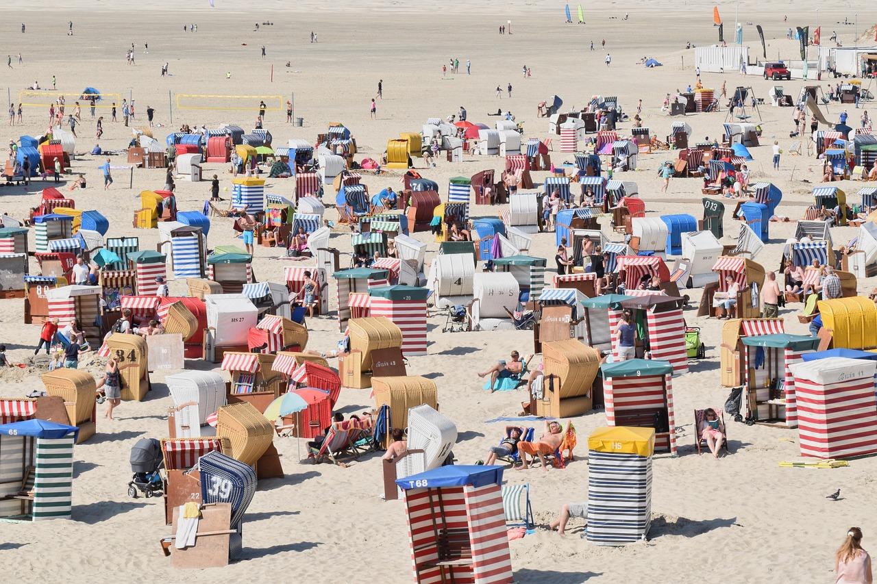 Słoneczna, zatłoczona plaża pełna kolorowych krzeseł plażowych i wypoczywających ludzi.