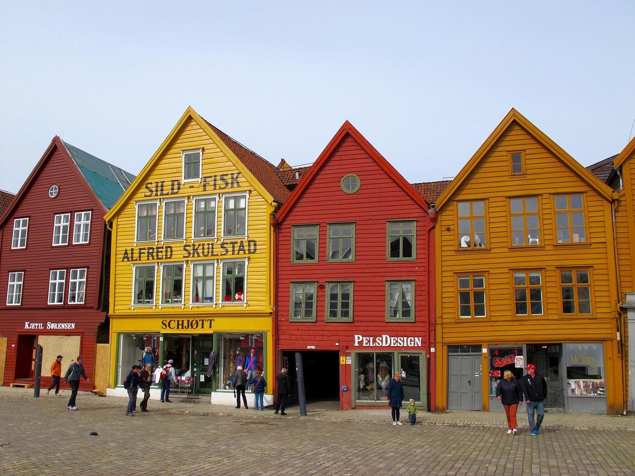 Kolorowe drewniane domy Bryggen w Bergen, Norwegia, z ludźmi na brukowanej ulicy.